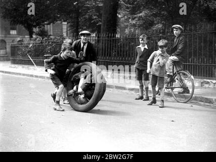 Les enfants jouent avec un vieux pneu surveillé par d'autres garçons. 1934 Banque D'Images