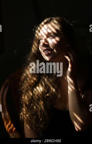 Portrait d'une femme européenne américaine assise sur une chaise, ombres à rayures. Banque D'Images
