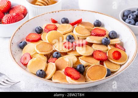 Petites crêpes avec fraises et bleuets pour le petit déjeuner. Mise au point sélective. Banque D'Images