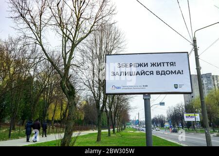 Ukraine, Lviv - 28 mars 2020: Panneau avec les mots "Save Lives! Restez à la maison ! » et des gens qui marchent. Publicité sociale à bord Banque D'Images