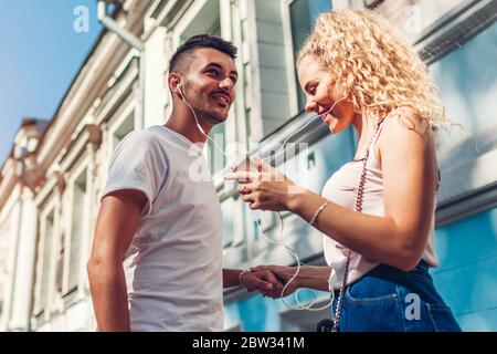Couple de course mixte amoureux écouter la musique au téléphone et danser dans la rue en ville à l'aide d'écouteurs. Banque D'Images