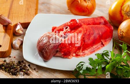 Poumons d'agneau crus et coeur sur table en bois avec herbes, oignon et ail Banque D'Images