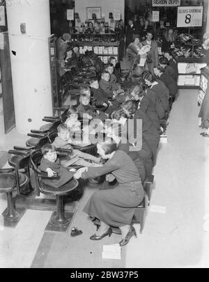 Service de masse pour la grande famille de l'Anglais déporté lorsqu'ils ont équipé de vêtements anglais dans le West End . M. George Shute , qui vient de rentrer en Angleterre avec sa femme et ses dix enfants après une longue période de chômage en Amérique , a visité Selfridges où lui et sa grande famille ont été équipés de vêtements anglais . Photos ; Service de masse pour les dix enfants de M. George Shute dans le département de la chaussure où toute la famille a été équipée de chaussures en un temps record de cinq minutes . M. et Mme Shute sont vus debout à l'arrière avec leur bébé de neuf semaines. 21 décembre Banque D'Images