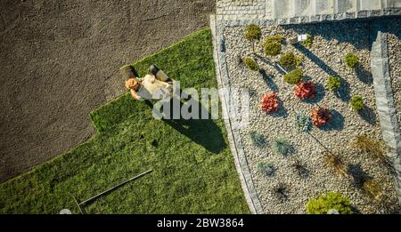 Aménagement paysager et jardinage. Vue aérienne du jardinier installation de l'herbe neuve dans le nouveau jardin résidentiel. Thème industriel. Banque D'Images