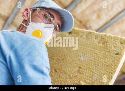 Entrepreneur travailleur portant un masque respiratoire sûr avec une pièce de laine minérale isolant intérieur matériau en mains. Rénovation et amélioration de la maison thème. Banque D'Images