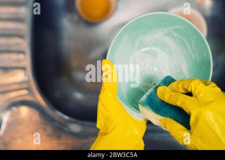 Les mains dans des gants de protection tiennent une éponge avec du détergent et lavez une plaque sur l'évier dans la cuisine, en gros plan Banque D'Images