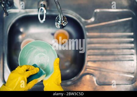 plaques de lavage en gants jaunes de protection sur le fond d'un évier vide dans la cuisine Banque D'Images