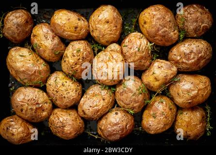 Pommes de terre entières cuites au four avec assaisonnement et herbes dans un plateau métallique. Pommes de terre rôties en vestes. Banque D'Images