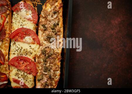 Longues baguettes de pizza avec thon, champignons, tomates et fromage sur un plateau métallique Banque D'Images