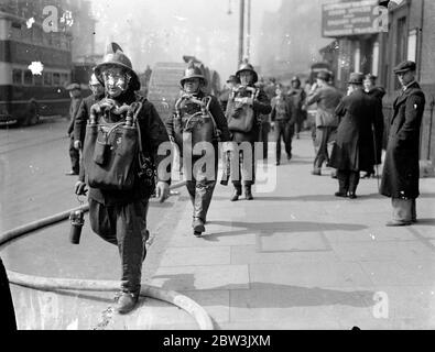 Des pompiers masqués au gaz combattent un grand feu au dépôt ferroviaire de Brickmavers Arms . Un des plus grands incendies que Londres a vu depuis un certain temps éclate au dépôt d'armes Brickmavers du Southern Railway . Le feu a commencé dans un hangar et s'est propagé à d'autres bâtiments . Des centaines de pompiers ont combattu les flammes tandis que les gens vivant à proximité ont sorti leurs meubles . Expositions de photos , pompiers avec gaz et appareil de fumée sur la scène du feu . 4 mai 1936 Banque D'Images