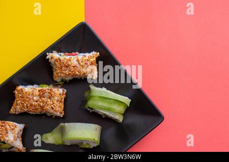 Vue de dessus en gros d'une assiette de sushis avec graines de sésame et enveloppement au concombre sur une combinaison de couleurs vives rose et jaune. Zone droite gauche pour cop Banque D'Images