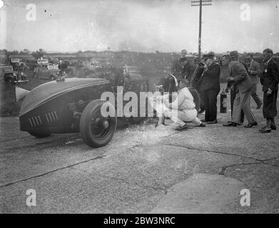 La voiture saute et éclate dans les flammes dans Big Race à Brooklands la Leyland - voiture Thomas conduite par R . J . Munday dans la course de Trophée d'Or , l'événement principal à la réunion de lundi de Pentecôte de Brooklands , a explosé et a éclaté en flammes à grande vitesse . Avec la voiture ablaze , Munday a roulé sur environ un demi-mile jusqu'à ce qu'il atteigne gangway où les tentatives ont été faites pour mettre hors de l'incendie . Munday a aidé dans la lutte . Spectacles photo : R . J . Munday ( en blanc ) aidant à combattre les flammes de sa voiture flamboyante . 1er juin 1936 Banque D'Images