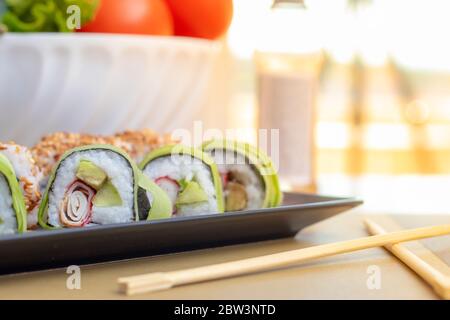 Petits pains à sushis faits maison de la californie et du concombre avec de la fausse viande de crabe surimi, de l'avocat et des graines de sésame frites. Servi en deux rangées sur une assiette noire à la maison. Banque D'Images