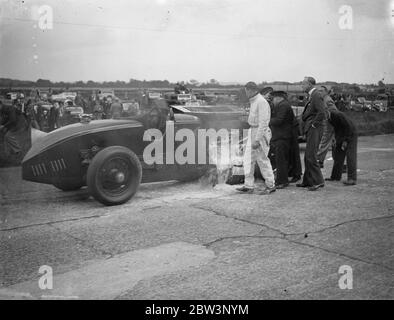 La voiture saute et éclate dans les flammes dans Big Race à Brooklands la Leyland - voiture Thomas conduite par R . J . Munday dans la course de Trophée d'Or , l'événement principal à la réunion de lundi de Pentecôte de Brooklands , a explosé et a éclaté en flammes à grande vitesse . Avec la voiture ablaze , Munday a roulé sur environ un demi-mile jusqu'à ce qu'il atteigne gangway où les tentatives ont été faites pour mettre hors de l'incendie . Munday a aidé dans la lutte . Spectacles photo : R . J . Munday ( en blanc ) aidant à combattre les flammes de sa voiture flamboyante . 1er juin 1936 Banque D'Images