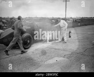 La voiture saute et éclate dans les flammes dans Big Race à Brooklands la Leyland - voiture Thomas conduite par R . J . Munday dans la course de Trophée d'Or , l'événement principal à la réunion de lundi de Pentecôte de Brooklands , a explosé et a éclaté en flammes à grande vitesse . Avec la voiture ablaze , Munday a roulé sur environ un demi-mile jusqu'à ce qu'il atteigne gangway où les tentatives ont été faites pour mettre hors de l'incendie . Munday a aidé dans la lutte . Spectacles photo : R . J . Munday ( en blanc ) aidant à combattre les flammes de sa voiture flamboyante . 1er juin 1936 Banque D'Images