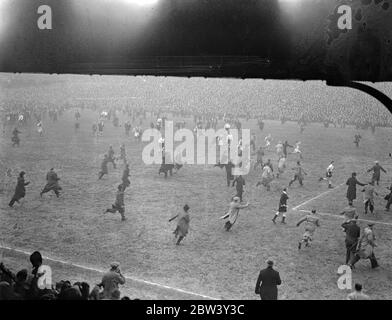 Les joueurs de Millwall fuient comme des milliers envahissent le terrain après la victoire de cravate de coupe . Les joueurs de Millwall devaient fuir du terrain lorsque des milliers de leurs supporters surjoints ont pris le terrain après la victoire de l'équipe sur Manchester City au sixième tour de la F A Cup à la « Den » , Nouvelle croix . Bientôt, tout le champ a été coincé avec des milliers de personnes . Des spectacles de photos , des joueurs de Millwall étant chassés sur le terrain par leurs admirateurs enthousiastes après le match . 6 mars 1937 Banque D'Images