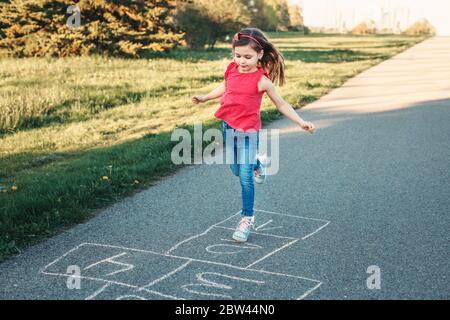 Adorable adorable adorable petite fille fille jouant à hopscotch en plein air. Jeu d'activités amusant pour les enfants sur l'aire de jeux à l'extérieur. Sports de rue d'arrière-cour d'été pour Banque D'Images