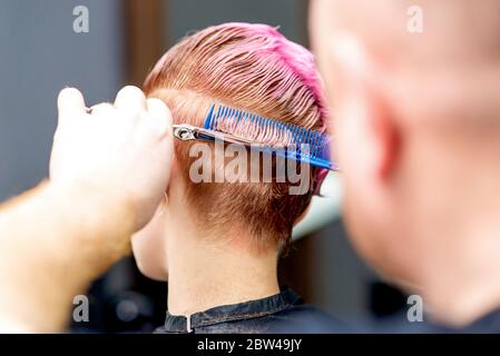 Vue arrière des mains du salon de coiffure couper femme cheveux courts, gros plan. Banque D'Images