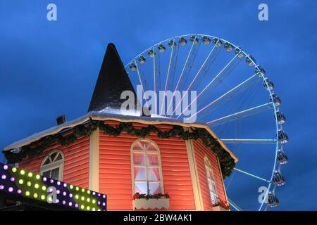 Grande roue illuminée la nuit, avec un stand de parc d'expositions, Winter Wonderland Hyde Park, Londres, Royaume-Uni Banque D'Images