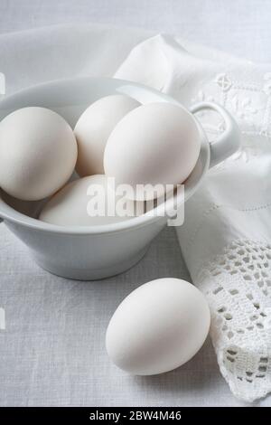 sur la nappe de lin blanc, au premier plan, un bol en céramique avec des œufs blancs frais prêts pour la préparation de recettes culinaires faites maison Banque D'Images