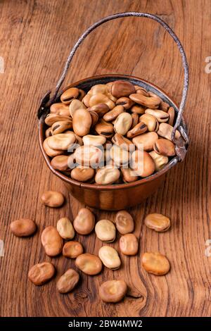 sur un fond en bois une casserole en cuivre avec des fèves séchées au premier plan Banque D'Images