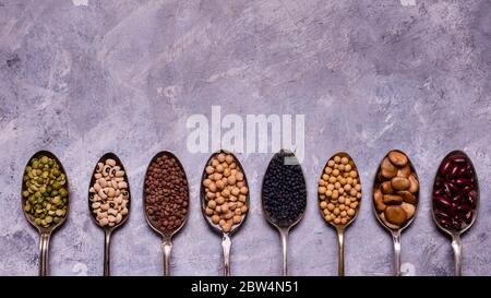 assortiment de légumineuses séchées en cuillères disposées en rangée avec vue du dessus sur fond texturé gris. espace pour les copies Banque D'Images