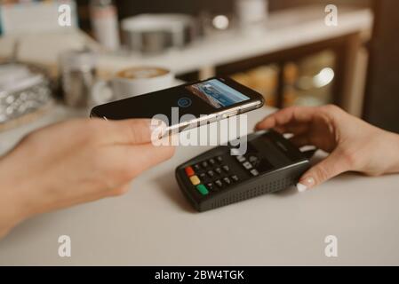 Une femme qui paie son Latte avec un smartphone grâce à la technologie de CARTE À PAIEMENT sans contact dans un café. Une femme barista tient un terminal pour payer à une cli Banque D'Images
