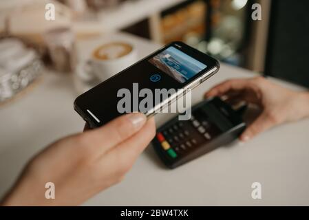 Une dame qui paie son latte avec un smartphone grâce à la technologie de CARTE à PAIEMENT sans contact dans un café. Une femme barista tient un terminal pour payer à un clié Banque D'Images