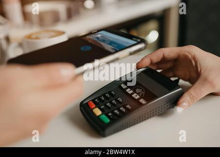 Une dame qui paie son latte avec un smartphone doté de la technologie NFC sans contact dans un café. Une femme Barista tient un terminal pour payer à un client dans Banque D'Images