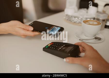 Une femme qui paie son Latte avec un smartphone doté de la technologie NFC sans contact dans un café. Une femme Barista tient un terminal pour payer à un client i Banque D'Images