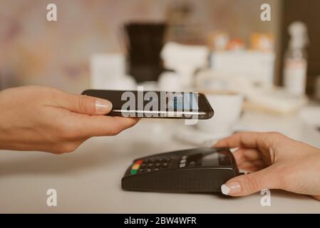 Photo rapprochée d'un smartphone se préparant à payer un latte par la technologie de CARTE À PUCE sans contact dans un café. Une femme Barista tient un terminal pour Banque D'Images