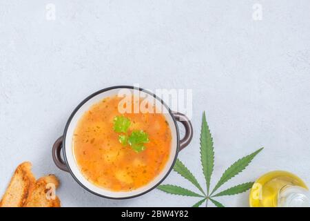 Concept alimentaire infusé au cannabis. Vue de dessus de la soupe de légumes de cannabis sur fond neutre avec feuille de marijuana, huile de cannabis, tranches de pain Banque D'Images