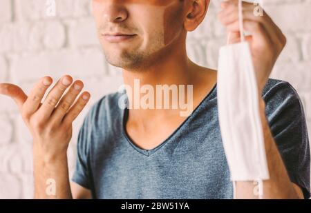 Portrait d'un jeune homme patient avec des lignes bronzées drôles sur le visage après avoir porté un masque médical. Un hipster homme confondu avec des coups de soleil et un visage peau Hol Banque D'Images