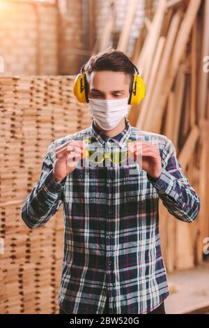 Portrait professionnel homme rufstman dans le masque médical et les protecteurs d'oreilles casque portant des lunettes de protection à la scierie. Menuisier confiant Banque D'Images