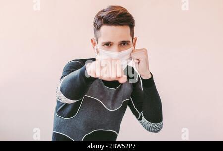 Portrait de jeune sportif agressif boxeur dans le masque médical faisant des exercices de boxe à la maison. Robuste homme de combat professionnel confiant dans prote Banque D'Images