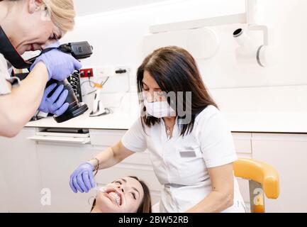 Dentiste photographiant la bouche d'une jeune patiente alors que l'infirmière tient sa bouche ouverte Banque D'Images