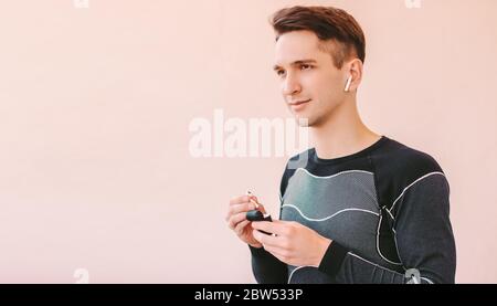 Portrait jeune sportif confiant, qui écoute de la musique avec des écouteurs sans fil et souriant. Un homme de fitness heureux avec des écouteurs bluetooth contre l'arrière-plan Banque D'Images