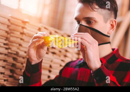 Gros plan du menuisier mâle dans un masque facial de protection portant des lunettes de protection lors de travaux à l'atelier de production de bois. Main-d'homme de l'armoire Banque D'Images