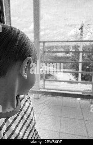 le garçon reste à la maison et regarde par la fenêtre. il manque ses amis et camarades de classe. Pendant la quarantaine, les enfants s'assoient à la maison en isolement. Banque D'Images