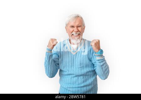 Libre. Homme barbu senior dans un chandail isolé sur les mains blanches dans les poings vers le haut souriant excité Banque D'Images