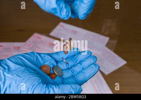 Pièces en euros tombant à la paume dans le gant de protection bleu, mandats sur le bureau en bois. Pertes économiques et financières. Pauvreté en cas de pandémie de coronavirus. Banque D'Images