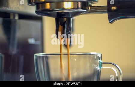 Gros plan deux flux de café expresso moussant sont versés dans une tasse de café en verre à partir de l'avertisseur de la cafetière. Banque D'Images