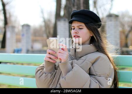Une fille surprise s'assoit sur un banc et regarde son téléphone Banque D'Images