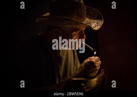 photo horizontale à faible clé d'un homme caucasien à l'aspect robuste éclairant une cigarette avec la flamme éclairant son visage avec l'espace de copie. Banque D'Images