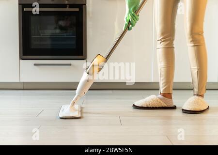 Femme en gants de caoutchouc utilisant un tampon de balai en microfibre et un flacon rechargeable avec une solution de nettoyage, en passant le sol dans l'appartement, en faisant des devoirs Banque D'Images