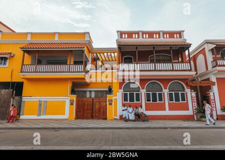 Quatre hommes sont assis sur un banc devant les bâtiments colorés de l'époque coloniale française à White Town, Pondichéry, Inde Banque D'Images