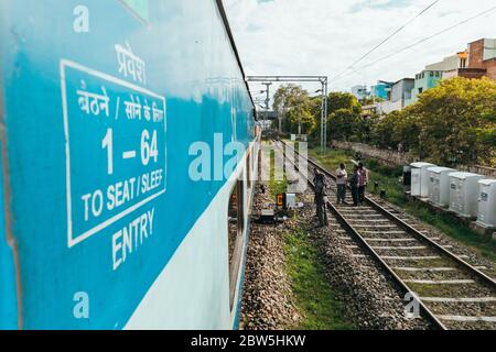 Les ingénieurs travaillent sur des voies ferrées, tandis qu'un train passe sur une voie adjacente à l'extérieur de Madurai, Tamil Nadu, Inde Banque D'Images