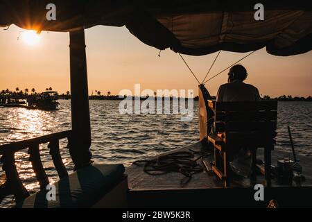 Le conducteur d'une péniche Keralan dirige le bateau depuis un siège sur l'arc, au coucher du soleil Banque D'Images