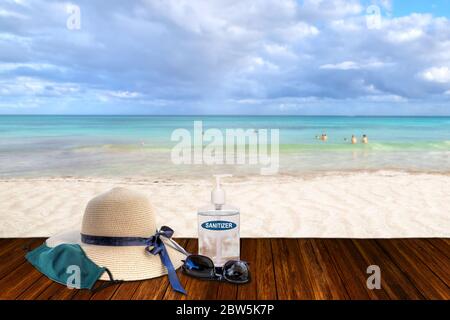 Vacances dans la nouvelle normalité après la pandémie du coronavirus COVID-19. Concept de tourisme montrant plage de sable avec chapeau de paille de plage, lunettes de soleil, aseptisant les mains Banque D'Images