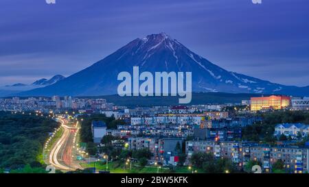 Panorama de la ville nocturne de Petropavlovsk-Kamchatsky sur fond cône du volcan, développement urbain au crépuscule, route de ville rétroéclairé avec voiture de conduite Banque D'Images